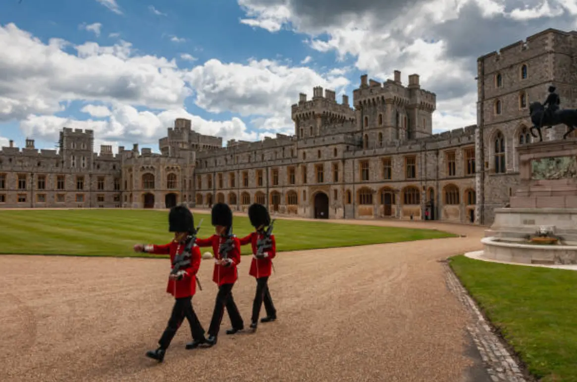 Guards in red uniforms marching in front of a grand historic castle