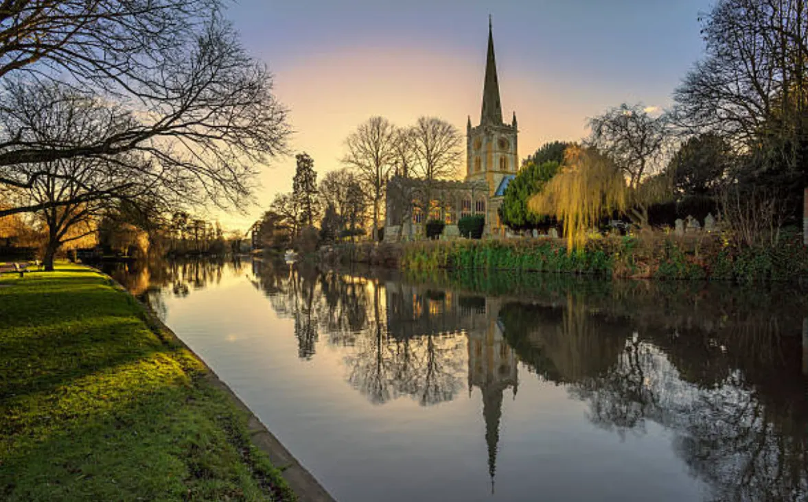 Vue sur la rivière depuis une église médiévale dont le clocher se reflète dans les eaux calmes du soir.