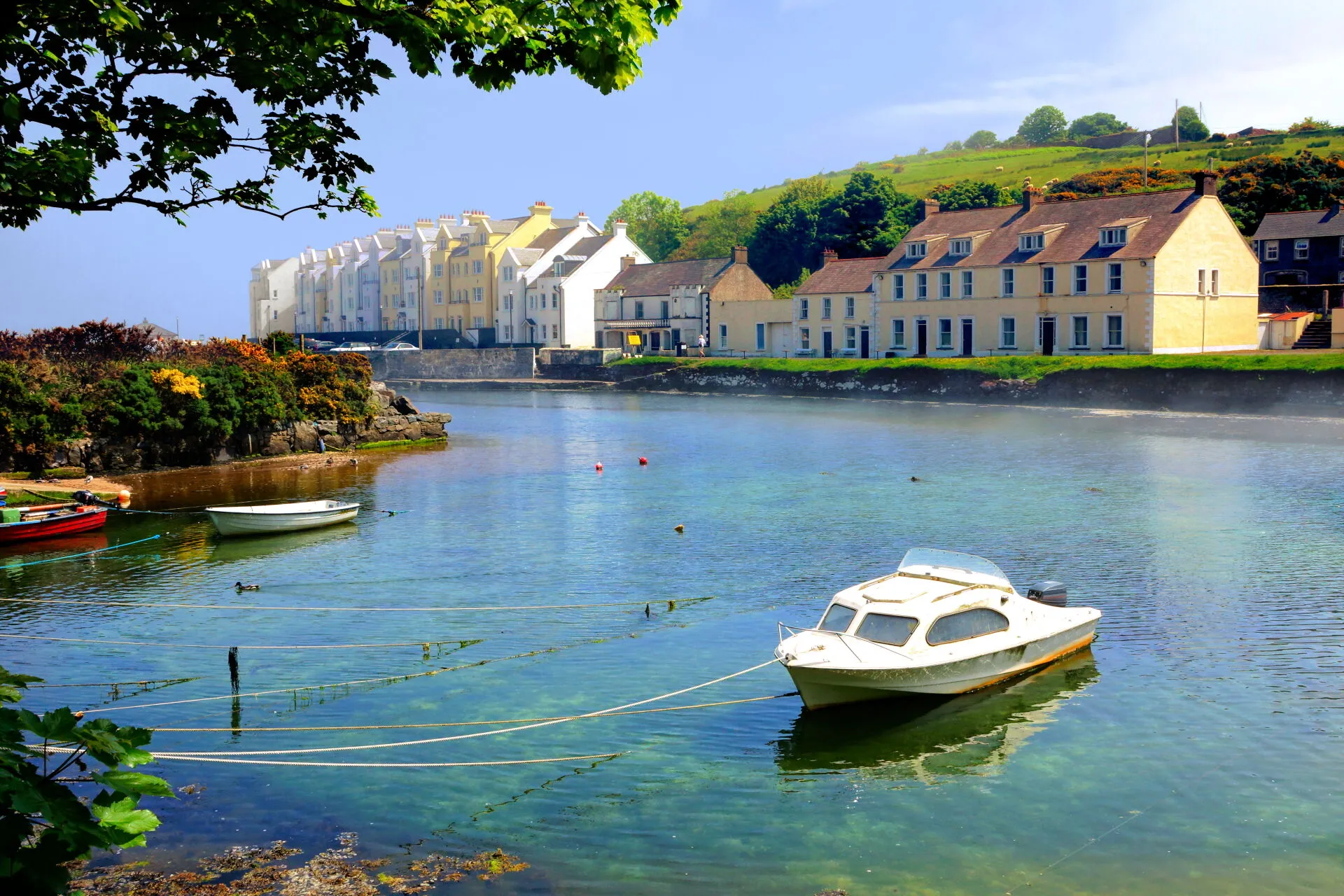 A serene view of white coastal cottages and small boats moored in the clear turquoise waters of Ballintoy Harbour on the Antrim Coast of Northern Ireland.