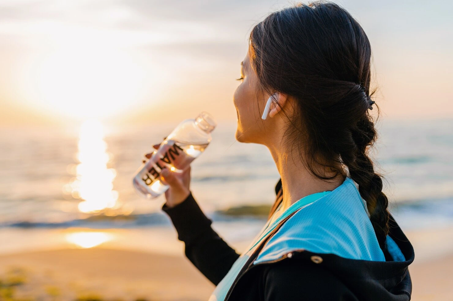 Active woman hydrating at sunrise by the sea during a wellness-focused travel experience