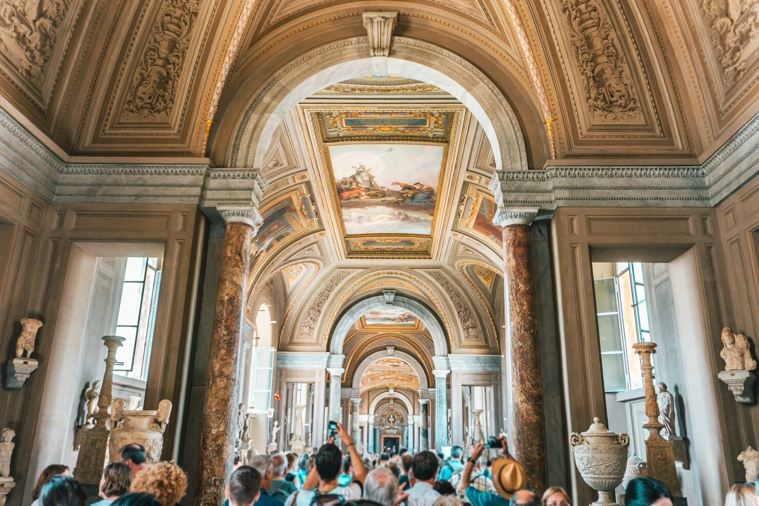 Visitors admiring ornate ceilings inside a historic Vatican museum gallery