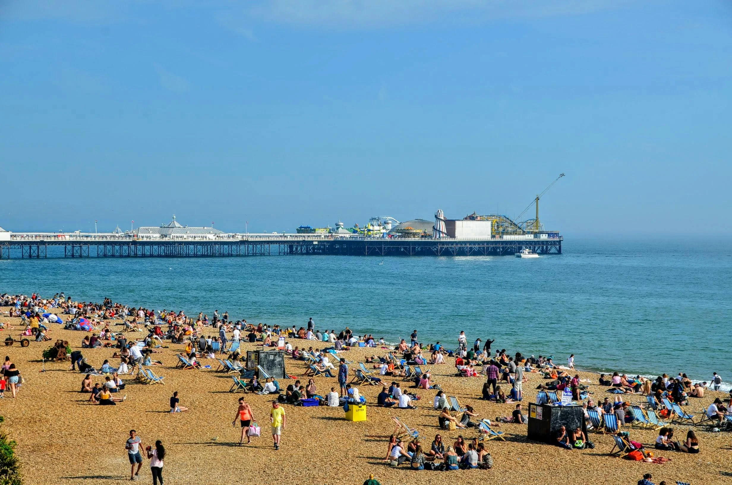 Brighton Beach crowded with sunbathers, with sandy shore and Brighton Pier in view.