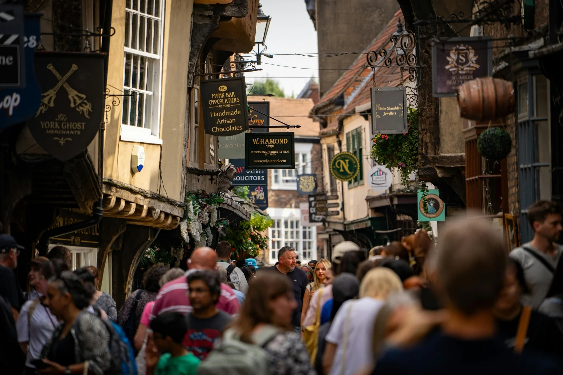 Busy street scene in York with shops, cafes, and crowds of people walking along The Shambles.
