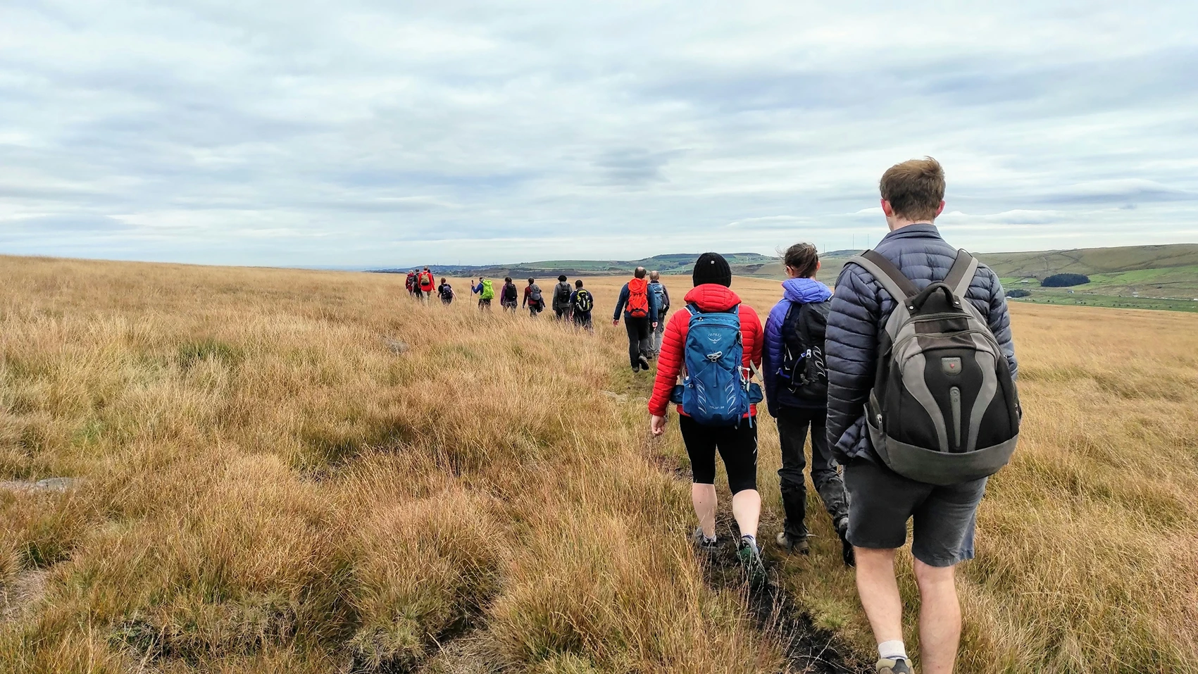 Walkers on the Cotswold Way above a valley village in late spring light