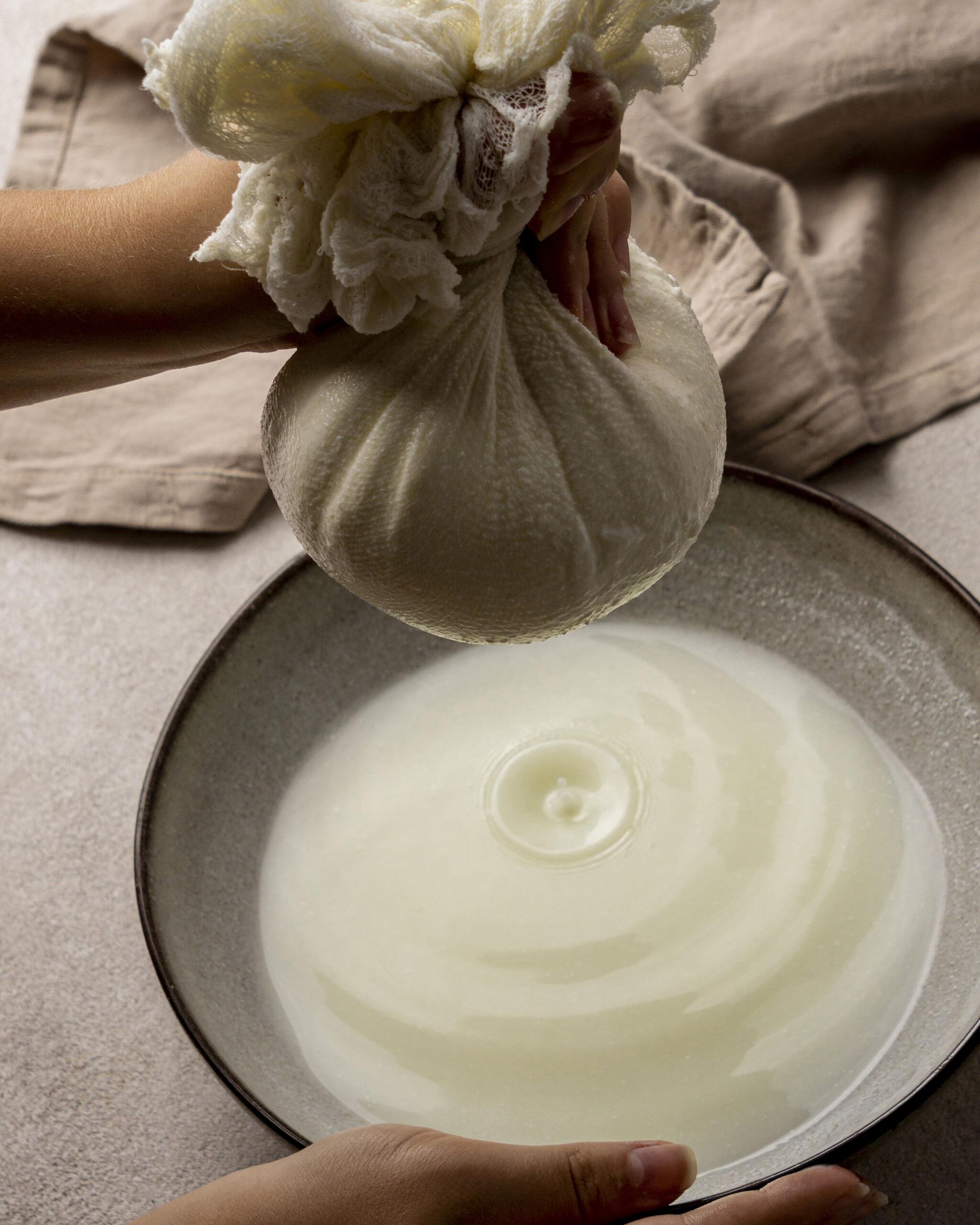 Artisan cheesemaker straining fresh cheese curds by hand in a cloth
