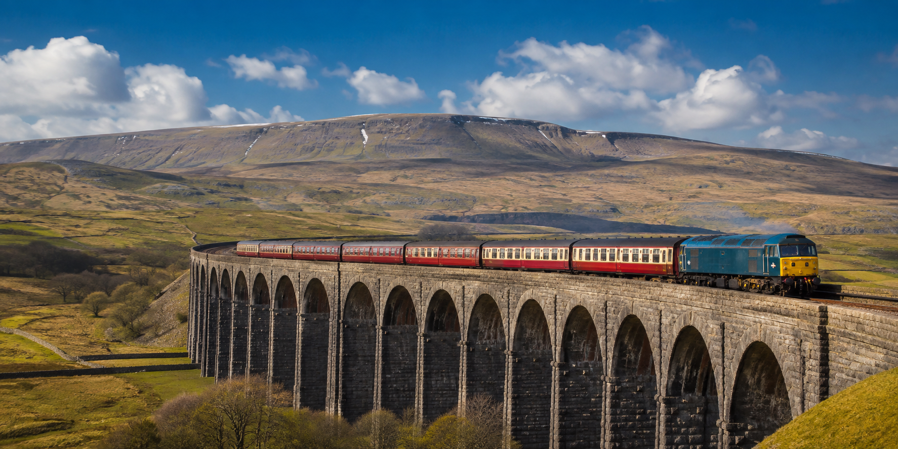 Train crossing a stone viaduct through rolling green hills on a scenic UK rail journey