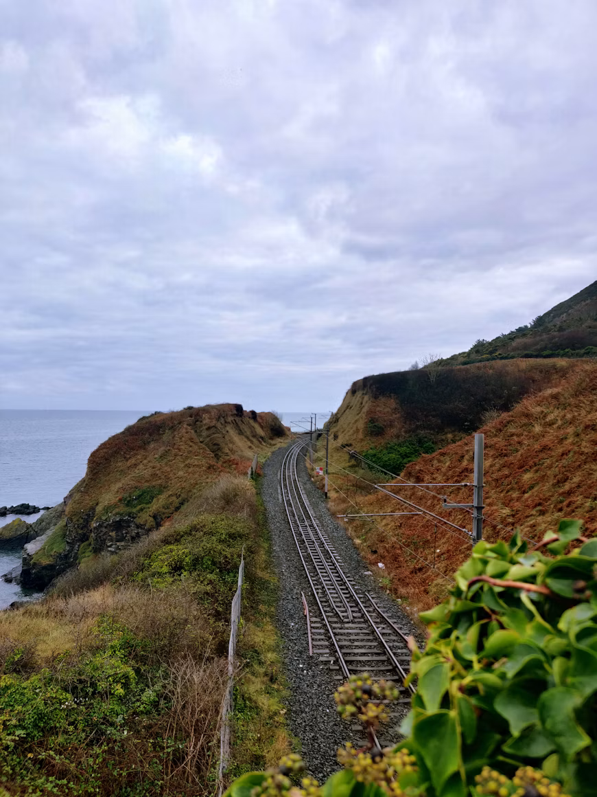 Coastal railway track curving along the Irish coastline under a cloudy sky