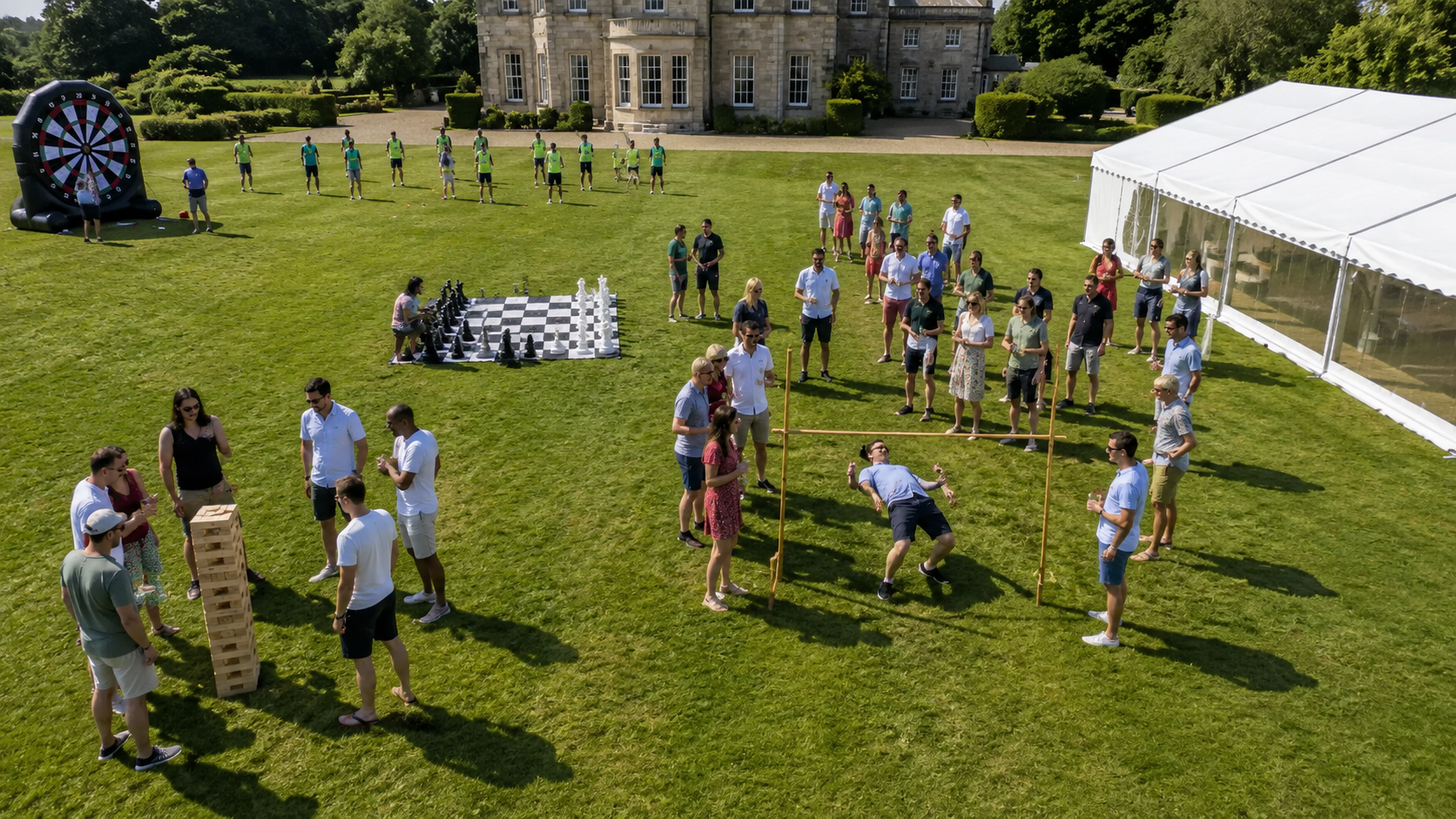 Corporate team building event taking place on the lawns of a grand English country estate with outdoor games and participants collaborating in natural daylight