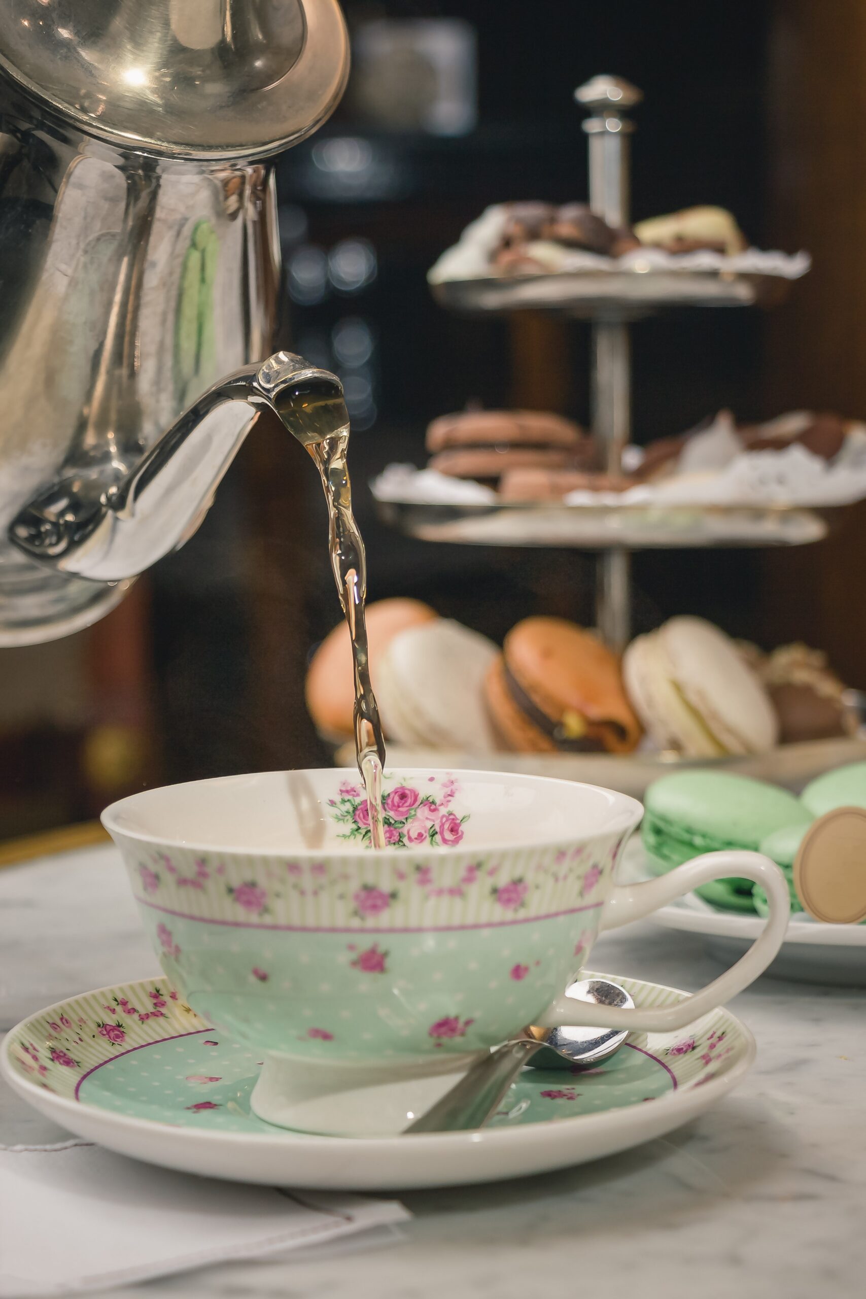 Traditional British afternoon tea with fine china teacup, freshly poured tea, macarons and a classic tiered cake stand.