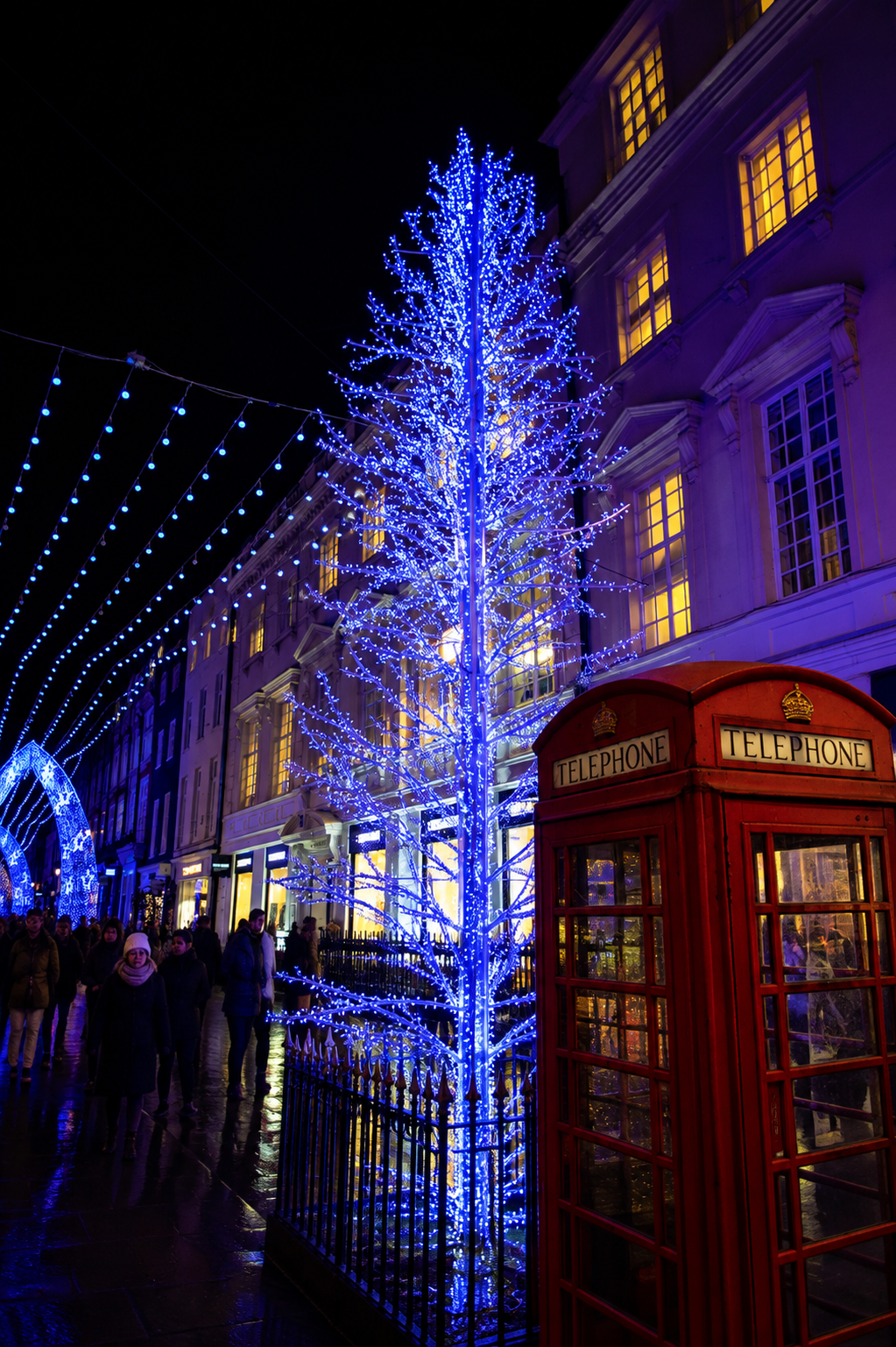 London street decorated with blue lights and a red phone box in winter